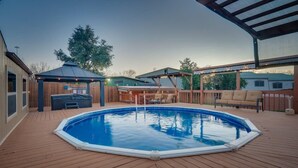 An outdoor swimming pool with a wooden deck, a hot tub, and a covered seating area.