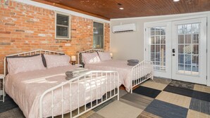 A room with two beds, a brick wall, an air conditioning unit, and a checkered floor.