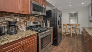 A modern kitchen with wooden cabinets, a stainless steel range, a black refrigerator, and a granite countertop.