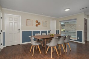 A dining area with a wooden table and grey chairs, a white door, and a window with a view.