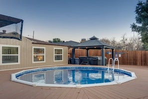 A backyard with a swimming pool, a covered patio, and a wooden fence.