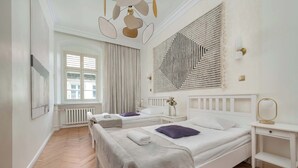 Une chambre d’hôtel avec deux lits, une commode blanche, une grande œuvre d’art abstraite accrochée au mur et une fenêtre avec des rideaux.