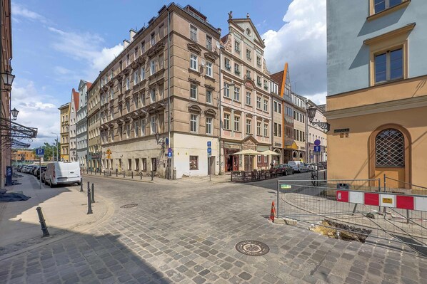 A multi-story building with a ground-floor commercial space, a cobblestone street, and a parked van.