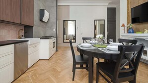 Une cuisine moderne avec des armoires blanches, un four encastré et un coin repas comprenant une table et des chaises en bois foncé.