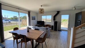 A spacious living area with a dining table, sofas, and a TV. There is a sliding glass door leading to a balcony with a view of the outside.