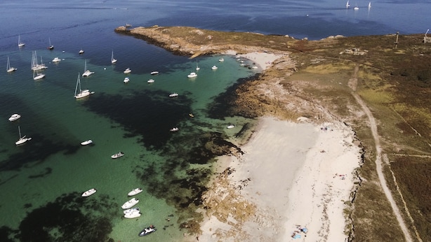 An aerial view of a coastal area with boats anchored near a sandy beach and rocky terrain.