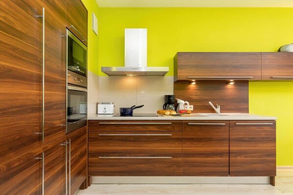 A modern kitchen with wooden cabinets, a stainless steel range hood, and a bright yellow wall.