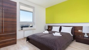 Ein Schlafzimmer mit einem großen Bett, einem Fenster, einem hölzernen Kleiderschrank und einer leuchtend gelben Wand.