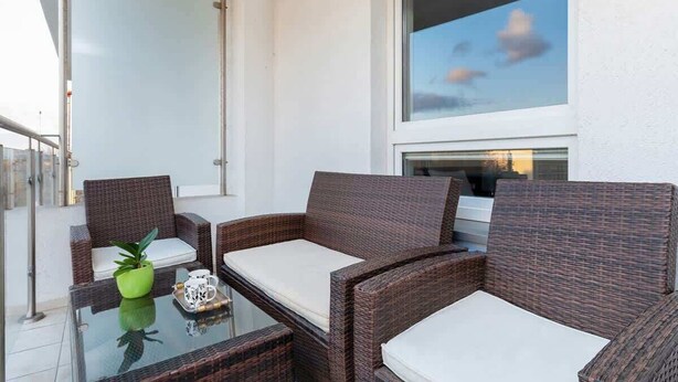 Ein Balkon mit Korbmöbeln, einem Glastisch und einem Blumentopf.