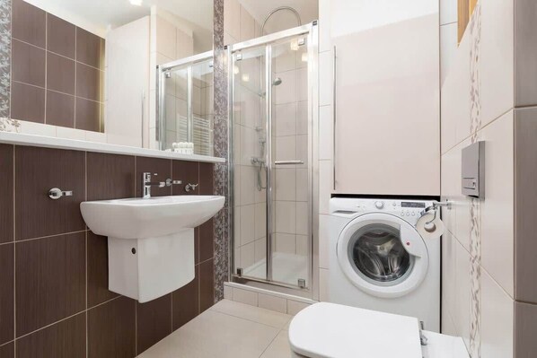 A bathroom with a sink, toilet, shower, and washing machine.