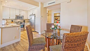 A modern kitchen with white cabinets, stainless steel appliances, and a dining area with wicker chairs and a glass table.