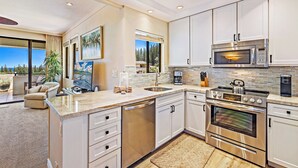 A modern kitchen with stainless steel appliances, white cabinetry, and a large window offering a view of the outdoors.