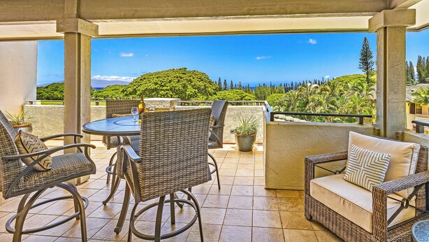 An outdoor patio with wicker furniture, a round table, and a view of a lush green landscape.