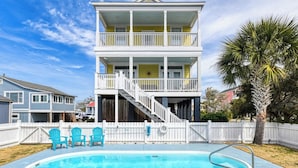 A two-story house with a balcony, a swimming pool, and a white picket fence.