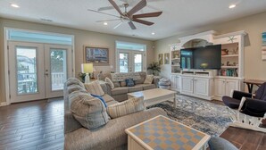 A spacious living room with a ceiling fan, a large TV, and a bookshelf.
