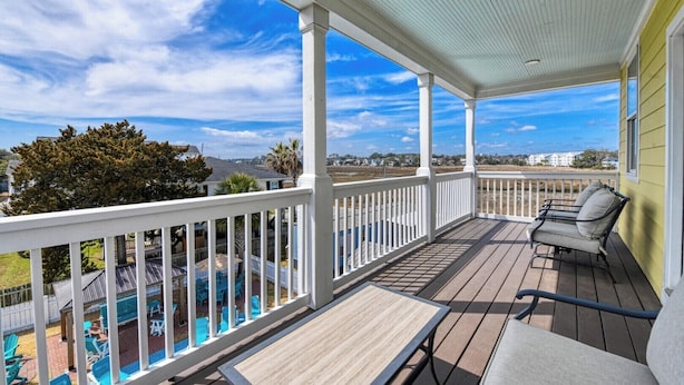 A covered outdoor deck with a view of a swimming pool and houses in the background.