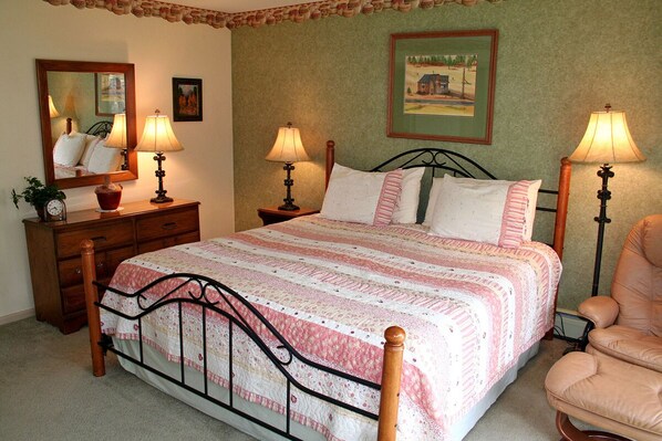 A bedroom with a bed, two bedside tables with lamps, a dresser, a chair, and a mirror.