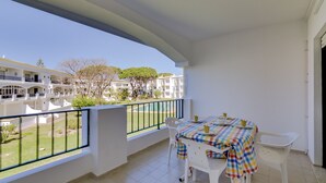Un balcon avec une table dressée pour deux personnes, donnant sur une cour intérieure bordée de bâtiments et d’arbres.