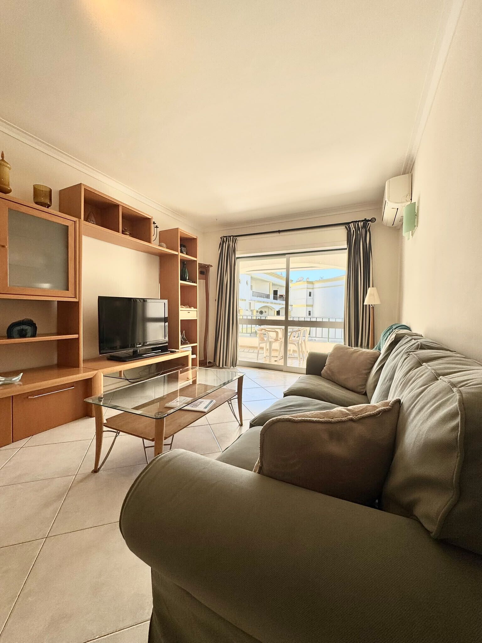 A living room with a sofa, TV, shelves, and a balcony view.
