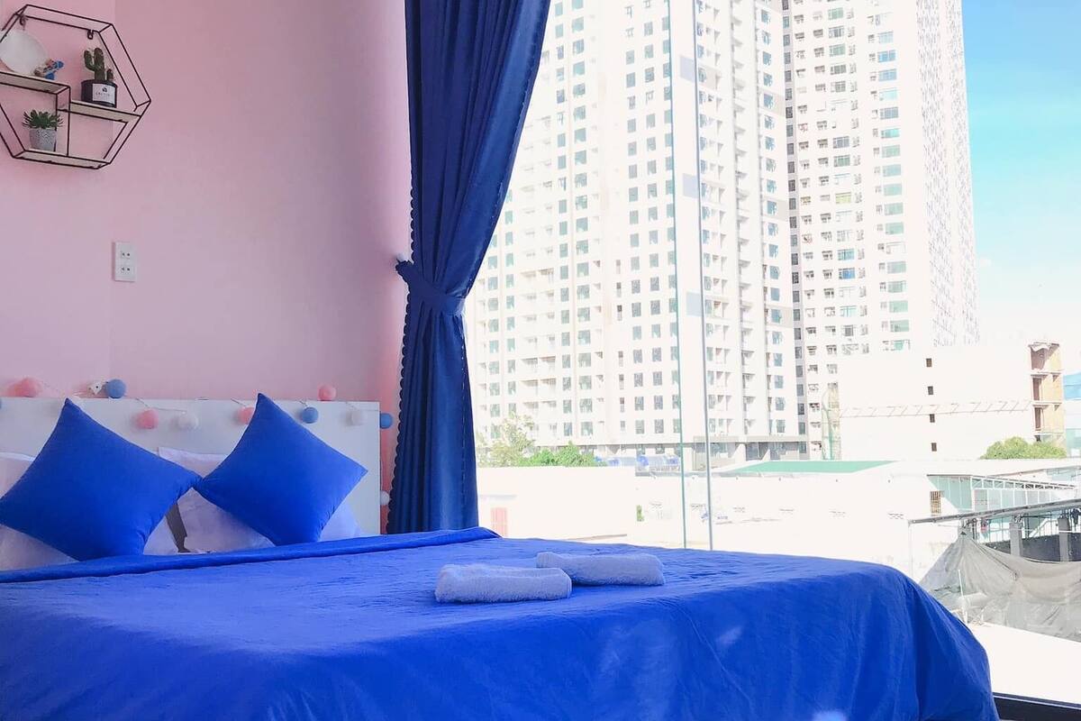 A modern bedroom with a large bed, a geometric wall decoration, and a view of a tall building through a window.