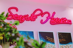 A neon sign reading "Seaside House" with three framed artworks depicting fish and underwater scenes. - Seaside House Homestay - Hostel (Bac Nha Trang)