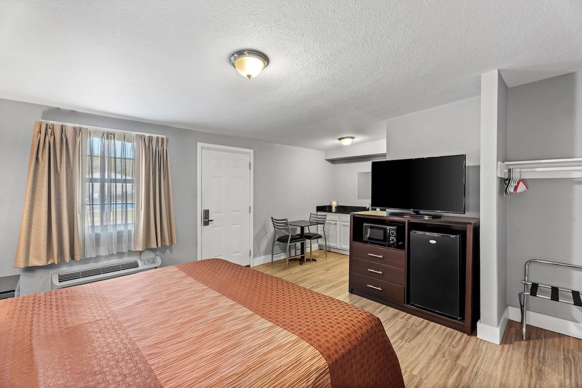 A hotel room with a bed, a desk, a television, a refrigerator, and a microwave.