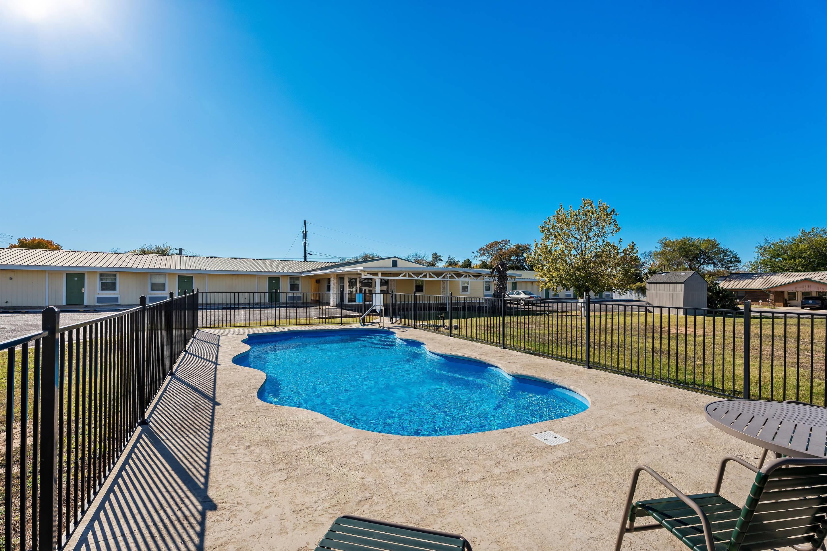 A swimming pool with a metal fence, a table and chairs, and a building in the background.