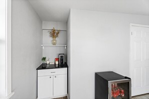 A white cabinet with a black countertop, a small shelf with a vase and a plant, and a refrigerator with soda cans. - Rodeway Inn Kingsland - Lake LBJ (Kingsland)