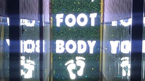 Un mur de verre orné d’enseignes lumineuses indiquant « Massage des pieds et du corps » et d’un symbole représentant une empreinte de patte.