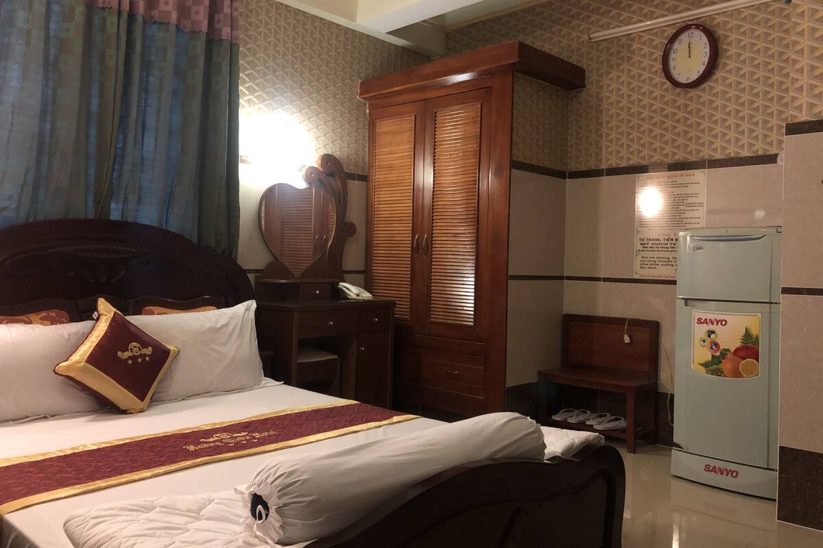 Une chambre d’hôtel équipée d’un lit, d’une armoire, d’un miroir, d’une horloge et d’un réfrigérateur.