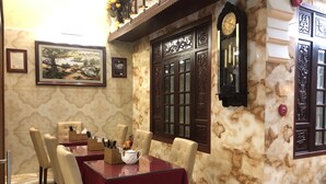 Un coin repas avec une table dressée pour quatre personnes, entourée de chaises. Il y a une horloge au mur et des œuvres d’art encadrées au-dessus de la table.