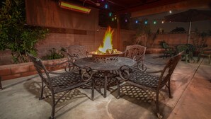 Eine Terrasse mit rundem Tisch, vier Stühlen, einer Feuerstelle und Lichterketten.
