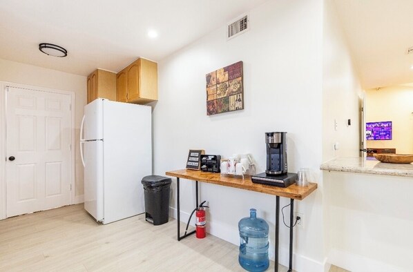 A compact kitchen with a white refrigerator, wooden cabinets, a coffee maker, and a water dispenser.