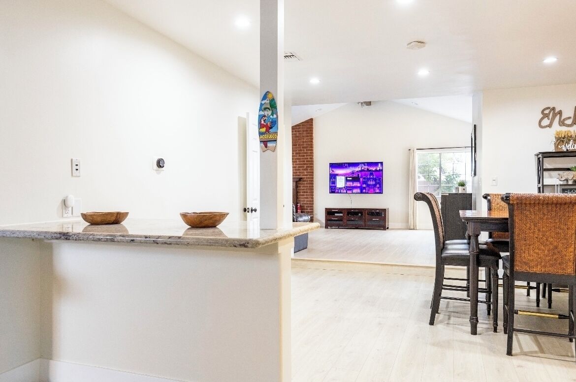 Una cocina moderna con una isla central, una zona de comedor con televisor y una pared de ladrillo decorativa.