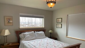 Une chambre à coucher avec un lit en bois, une table de chevet avec une lampe, une fenêtre avec des stores et un luminaire au plafond.