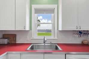 A kitchen with a stainless steel sink, white cabinets, a red countertop, and a window with a view of a lake and greenery.