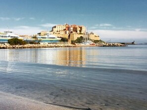 A coastal town with a prominent castle-like building, a calm sea, and a rocky shoreline. - Studio Orsoni - See View (Calvi)