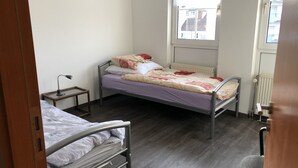 Une petite chambre avec un lit simple, une fenêtre, un radiateur et un bureau avec une lampe.