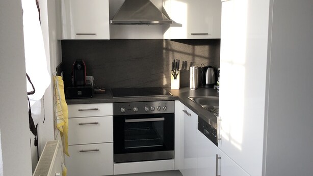 Une cuisine compacte avec des meubles blancs, un four encastré, un four à micro-ondes et une cuisinière à gaz.