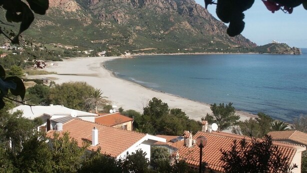 A coastal view with a beach, a mountain in the background, and residential buildings with red-tiled roofs. - Holiday Marina di Tertenia 150 meters from the sea IUN P2910 (Tertenia)