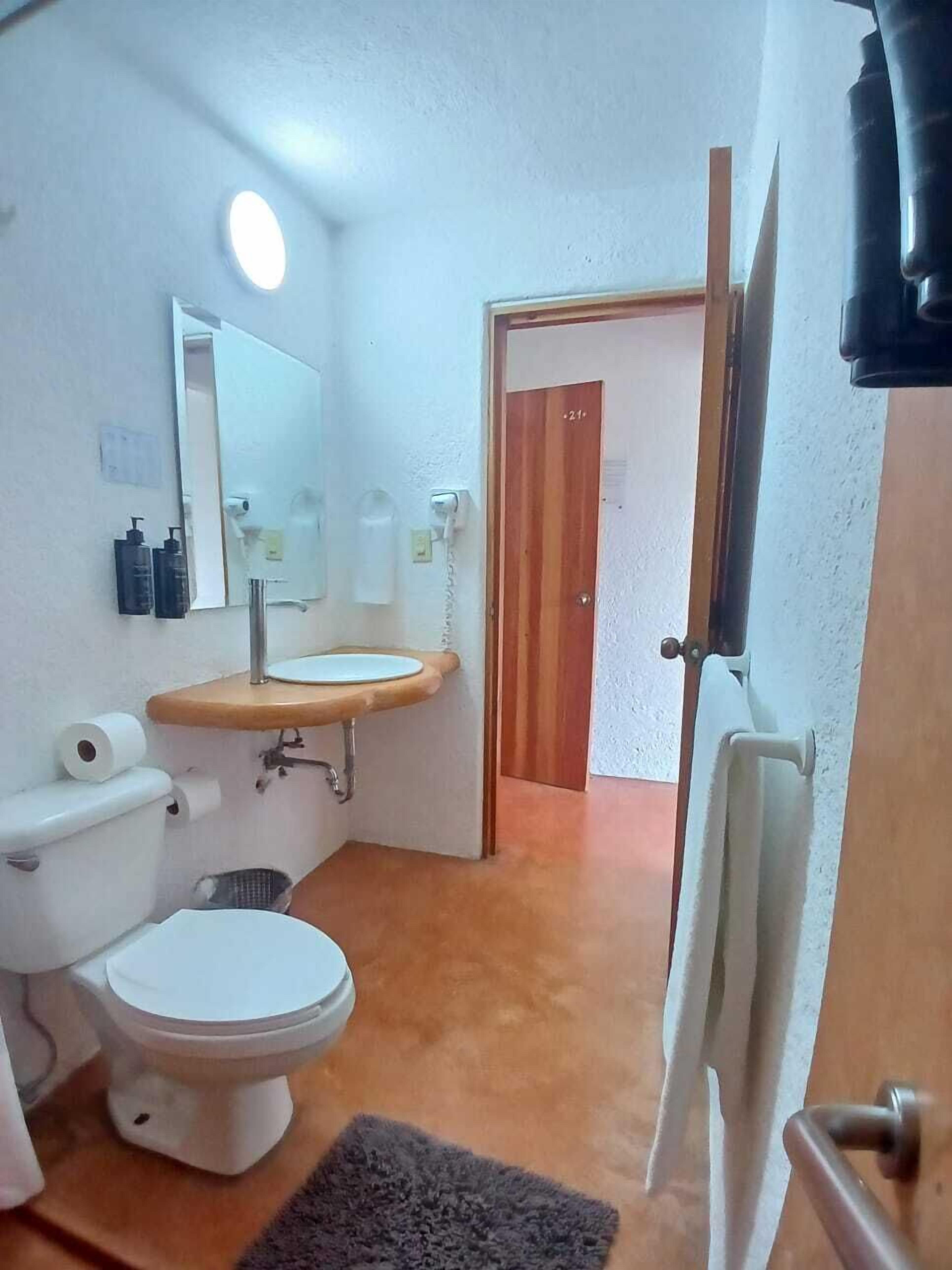 Une salle de bain comprenant des toilettes, un lavabo, un miroir et un espace douche.