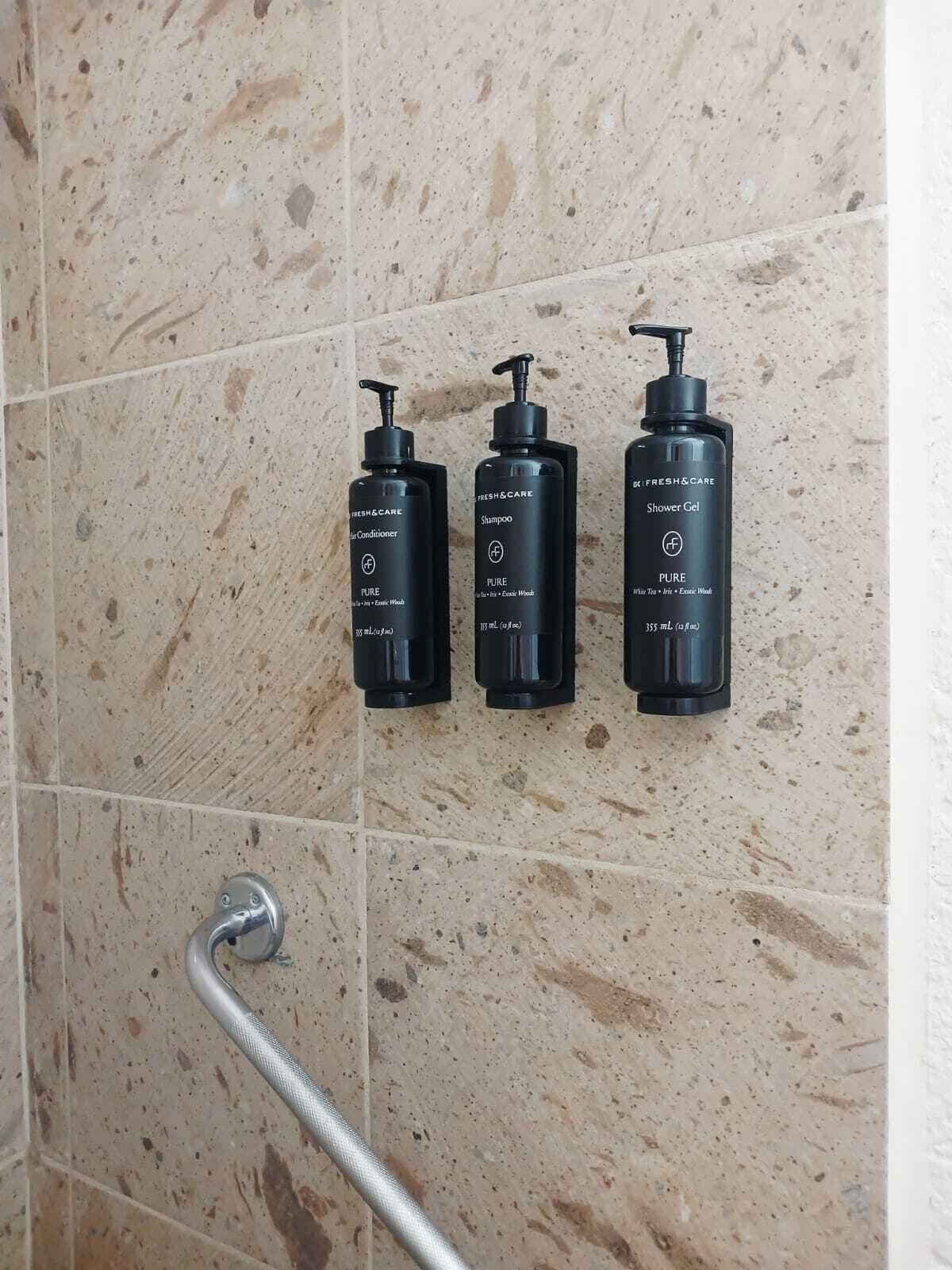 Drie zwarte flessen Fresh & Care producten op een betegelde muur.