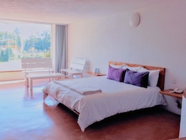Habitación de hotel con cama, una silla, una mesita y ventana con vista a árboles.