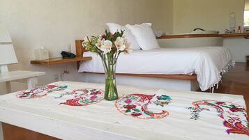 A hotel room with a bed, a bedside table, a nightstand, and a vase with flowers.