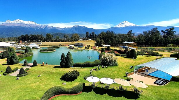 A resort with a large swimming pool, tennis courts, and a mountain backdrop.