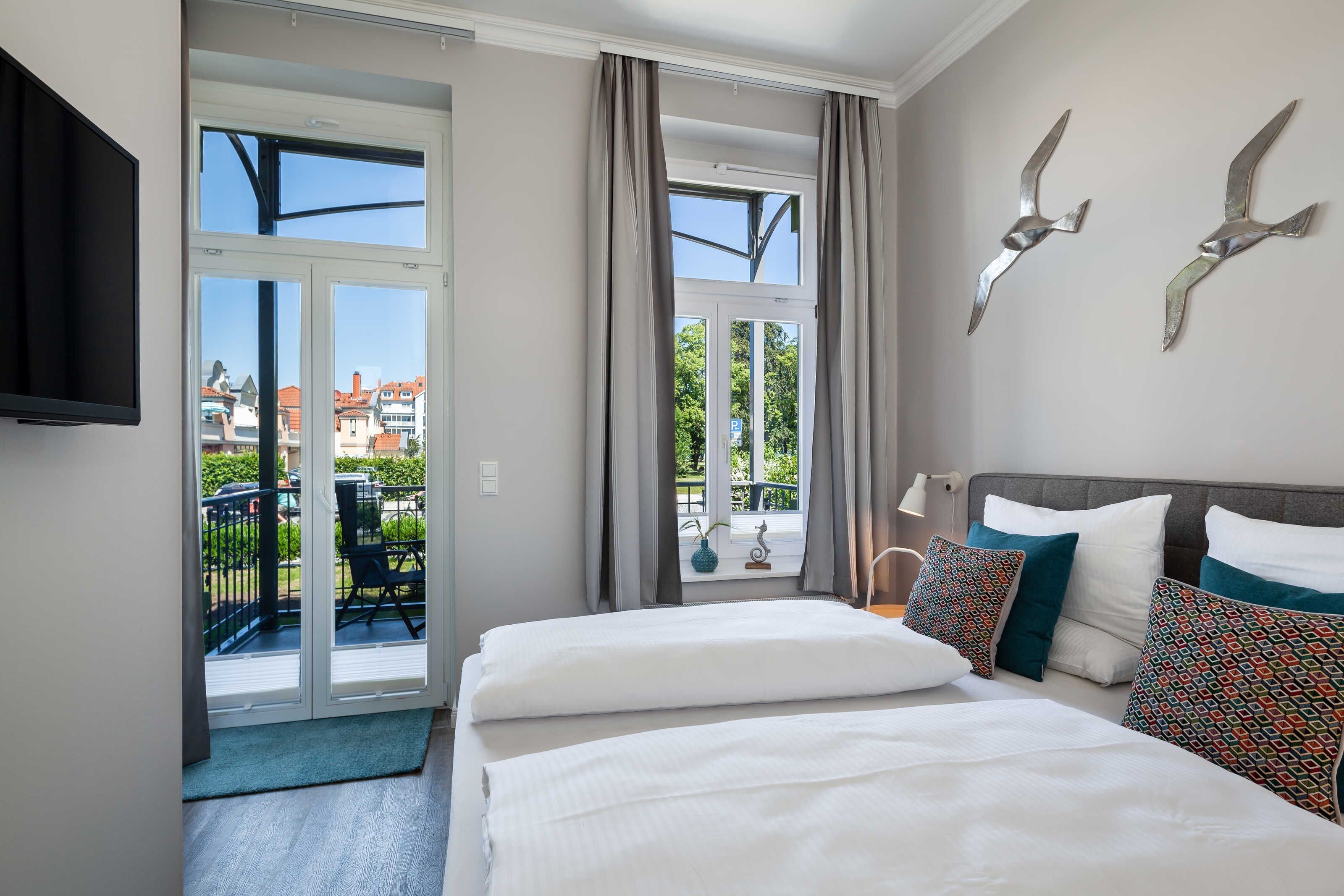 Een hotelkamer met balkon, een bed met witte beddengoed en decoratieve wandkunst.
