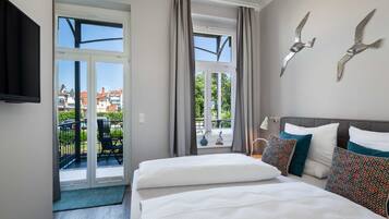 Een hotelkamer met balkon, een bed met witte beddengoed en decoratieve wandkunst.