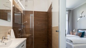 Un baño moderno con ducha envuelta en vidrio, lavamanos blanco y espejo.