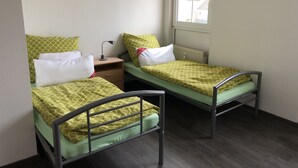 A dormitory room with two single beds, a nightstand, a desk, and a window. - Ferienwohnungen Popp (Clausen)