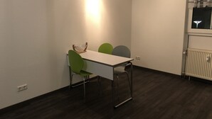 A small dining area with a white table and green chairs, a radiator, and a window with curtains. - Ferienwohnungen Popp (Clausen)